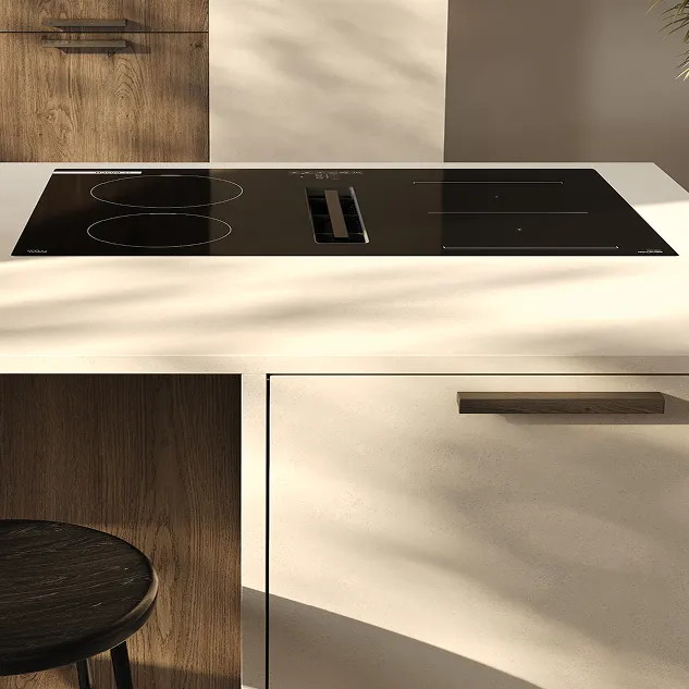 Schwarzes Induktionskochfeld in eine helle Kücheninsel integriert, umgeben von warmen Holzakzenten und beigem Frontdekor, zeigt moderne Küchengestaltung mit klaren Linien.